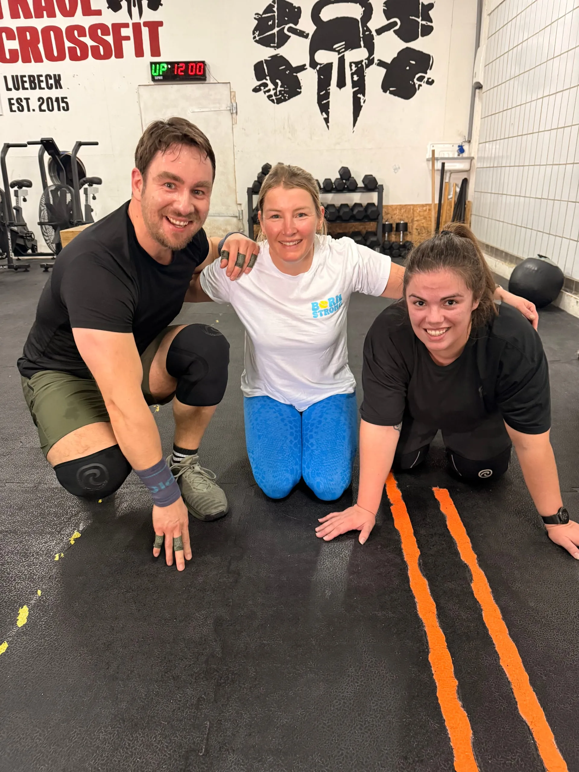 Three athletes crouching on the floor of the Trave CrossFit box, smiling at the camera
