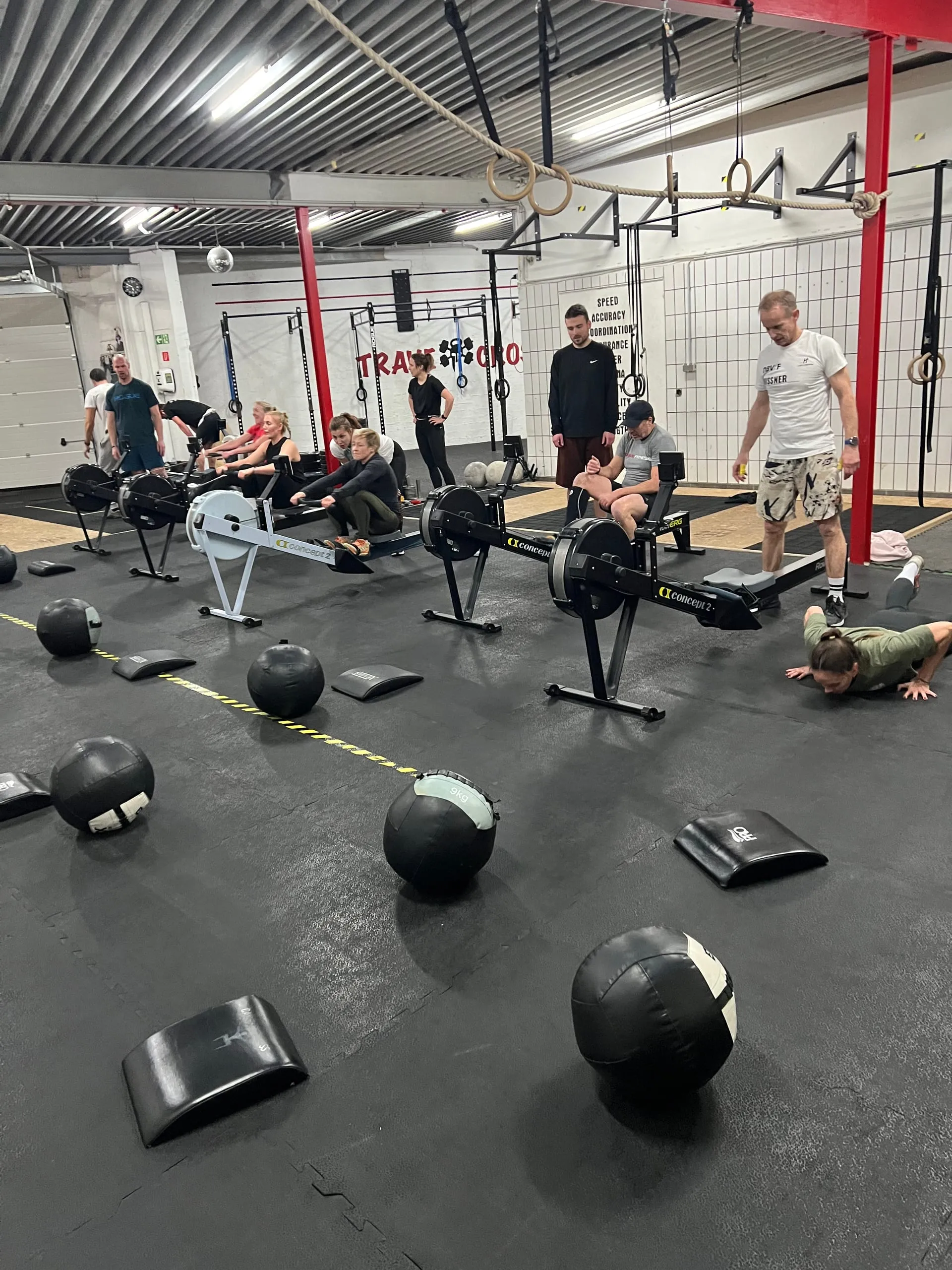 Group training on rowers, wall balls and mats laid out on the floor